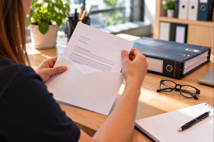 Handen openen een officiële brief op een bureau naast een gesloten ordner